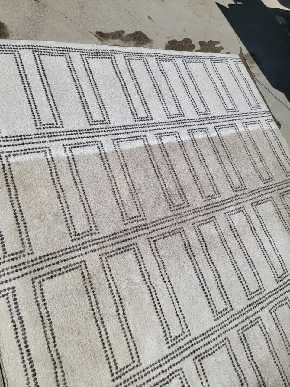 Ivory patterned rug, one half cleaned, laid on a driveway